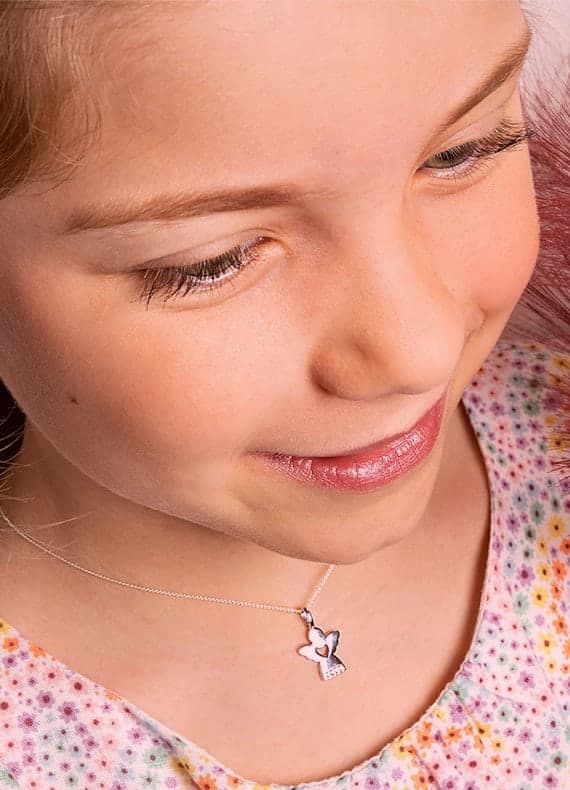 Mädchen im geblümten Shirt trägt eine feine Kette mit kleinem Engelanhänger um den Hals