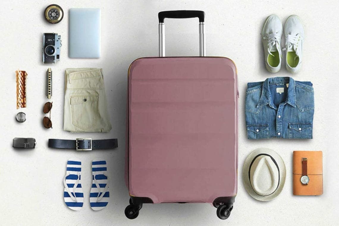 Rosa Rollkoffer von oben, umgeben von Reiseutensilien wie Kamera, Kleidung, Schuhen, Hut, Sandalen und Notizbuch