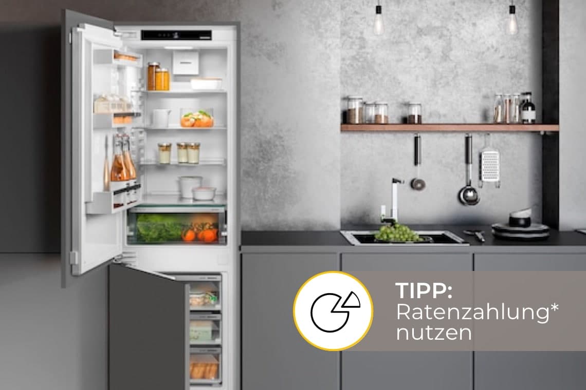 Tipp: Ratenzahlung nutzen – geöffneter Kühlschrank neben moderner grauer Küchenzeile mit Spüle und Obst auf der Arbeitsplatte