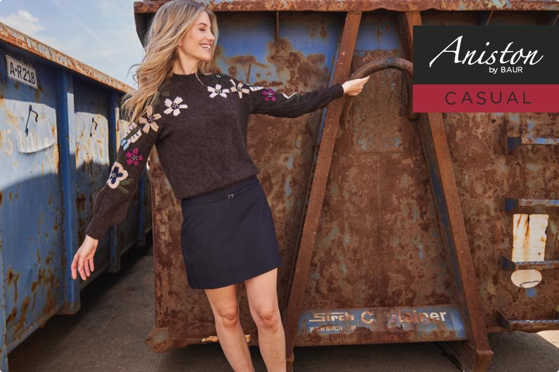 Aniston by Baur Casual – Frau im geblümten Pullover und kurzem Rock lacht vor einem rostigen Container
