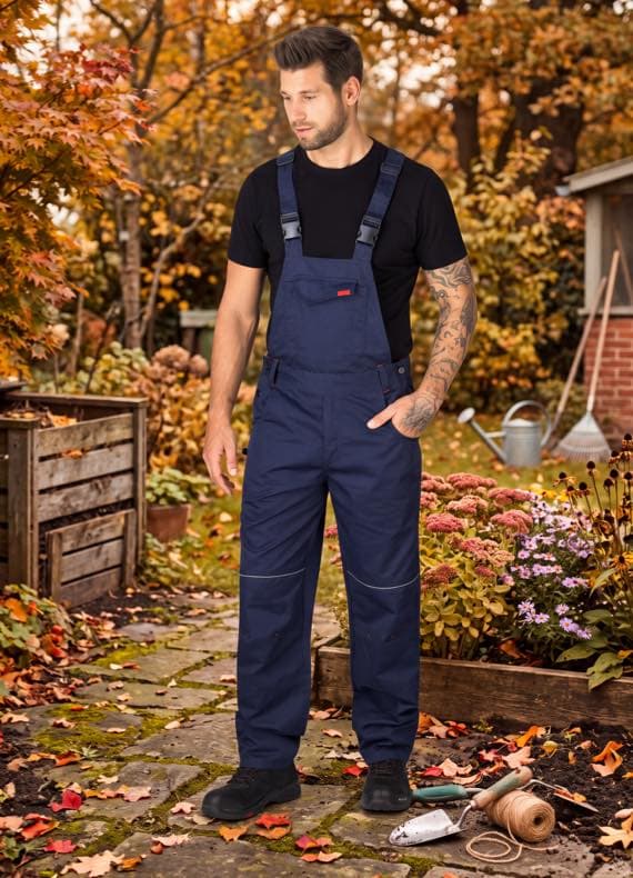 Mann in dunkelblauer Latzhose und schwarzem T‑Shirt steht im herbstlichen Garten zwischen Beeten und Gartengeräten