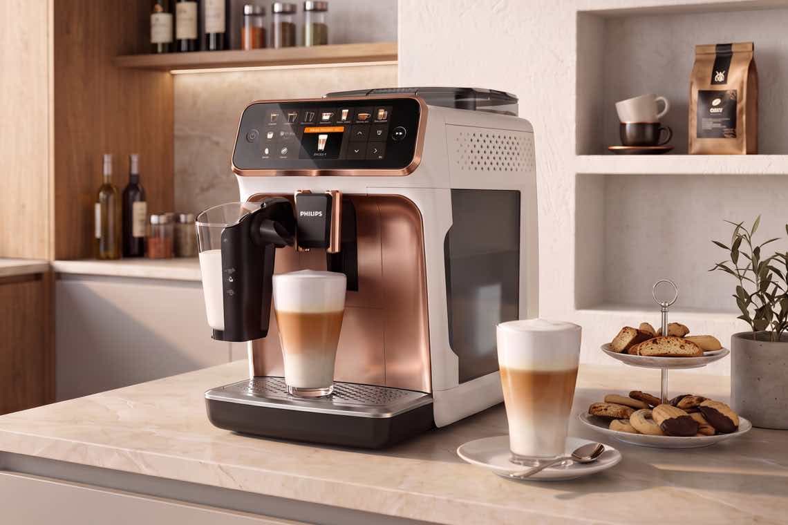 Kaffeevollautomat auf Küchenarbeitsplatte bereitet Latte Macchiato zu, daneben Glas mit Milch, weiteres Glas und Gebäcketagere