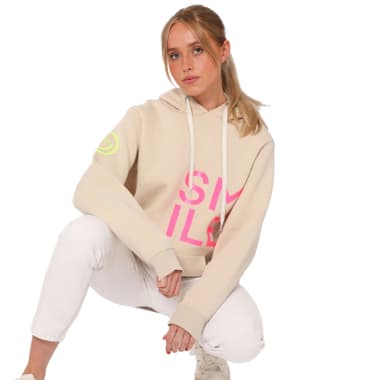 SMILE Schriftzug auf Hoodie – Frau in beigem Kapuzenpullover und weißen Jeans hockt im Studio
