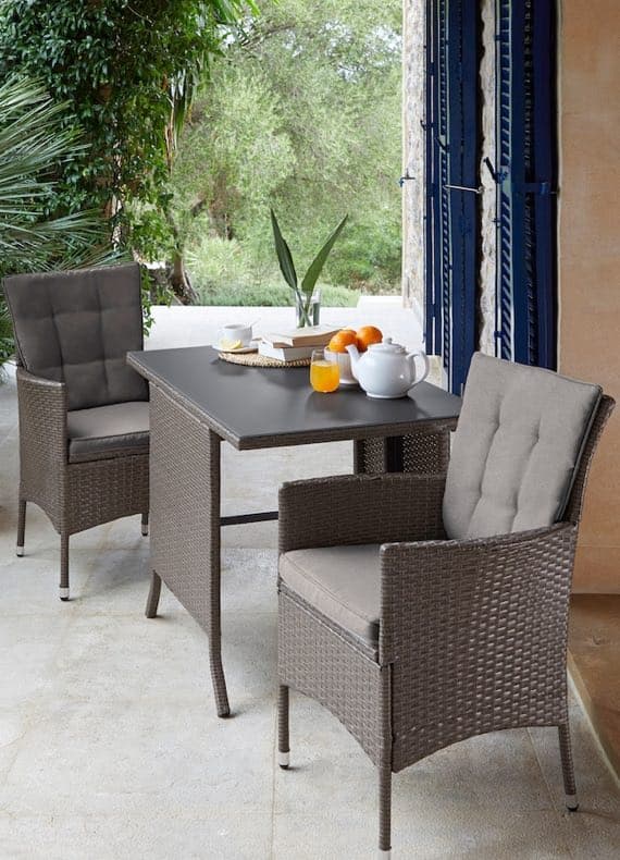 Gartentisch mit zwei Polsterstühlen, darauf Teekanne, Glas Saft, Tasse und Schale mit Orangen auf Terrasse mit Grünblick