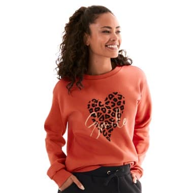 Pullover mit Herzmuster und Schriftzug "Love" – Frau mit lockigem Haar trägt roten Pullover und dunkle Hose