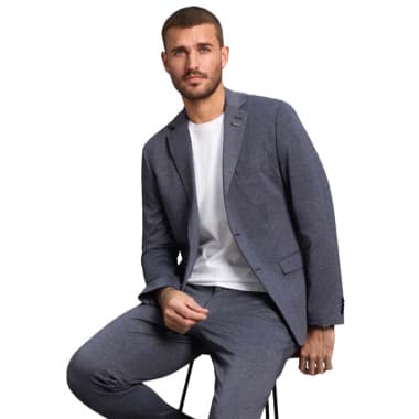 Mann in grauem Anzug mit weißem Shirt sitzt lässig auf einem Barhocker