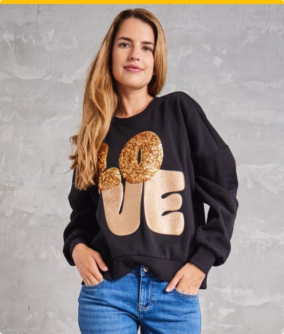 LOVE-Schriftzug auf schwarzem Pullover – Frau mit langen blonden Haaren trägt Pullover und blaue Jeans