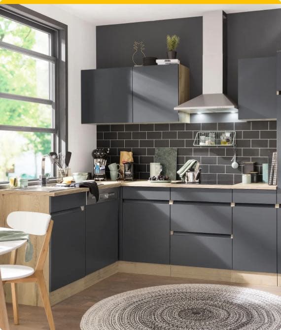 Moderne Küche mit dunkelgrauen Schränken, hellen Arbeitsplatten und großem Fenster. Kochutensilien und Pflanzen auf der Arbeitsfläche.