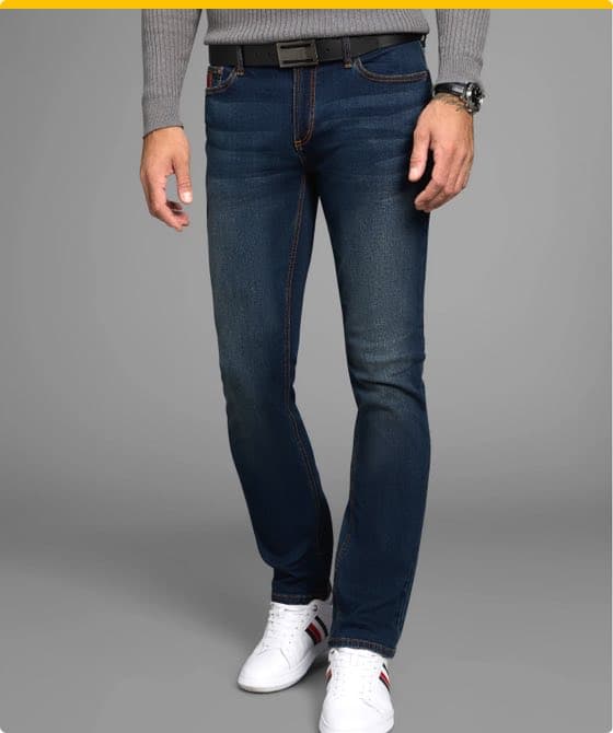 Mann in dunkelblauer Jeans und grauem Pullover, trägt weiße Sneakers mit roten und schwarzen Streifen, grauer Hintergrund