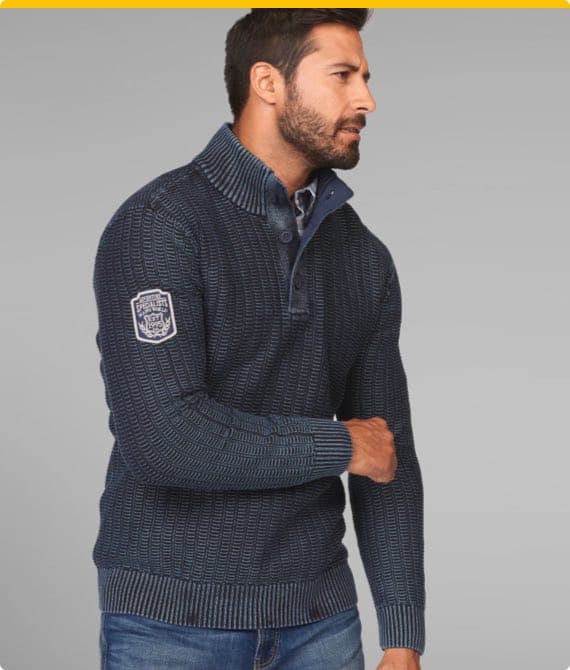 Mann in dunkelblauem Strickpullover mit Kragen und Knöpfen, Patch auf dem Ärmel, trägt blaue Jeans