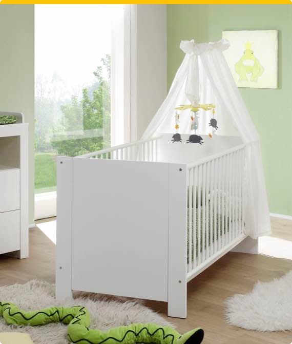 Weißes Babybett mit Baldachin und Mobile, daneben eine weiße Kommode, grünes Froschbild an der Wand und Spielzeug auf dem Boden