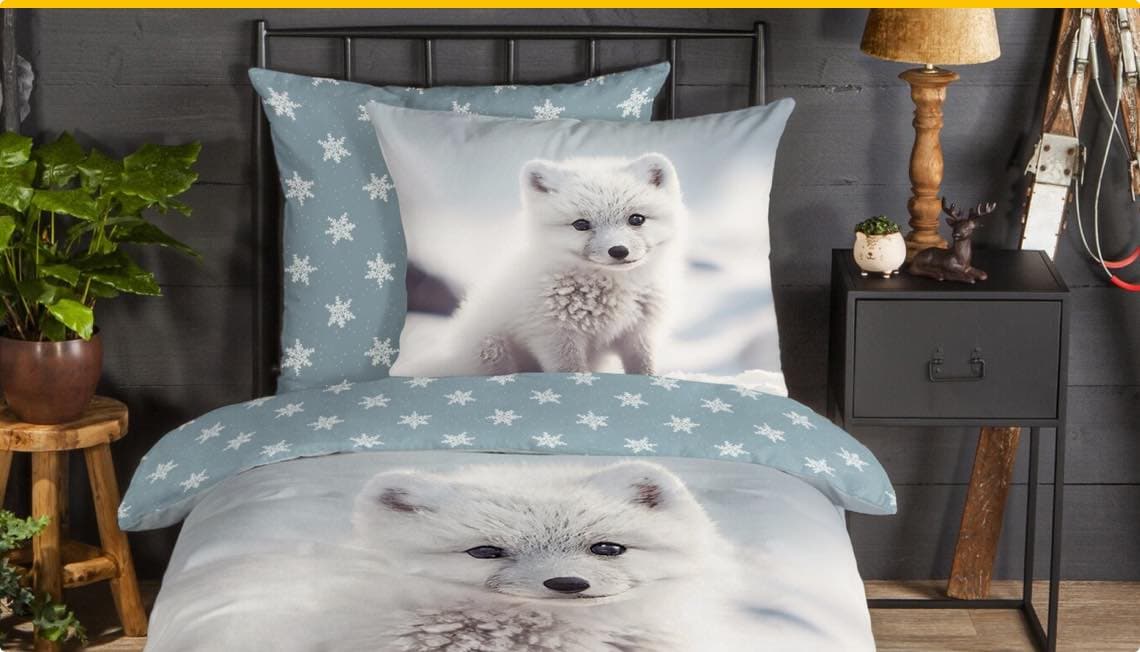 Bettwäsche mit Schneeflocken und Polarfuchs-Motiv auf Bett, daneben Nachttisch mit Pflanze und Dekorationen