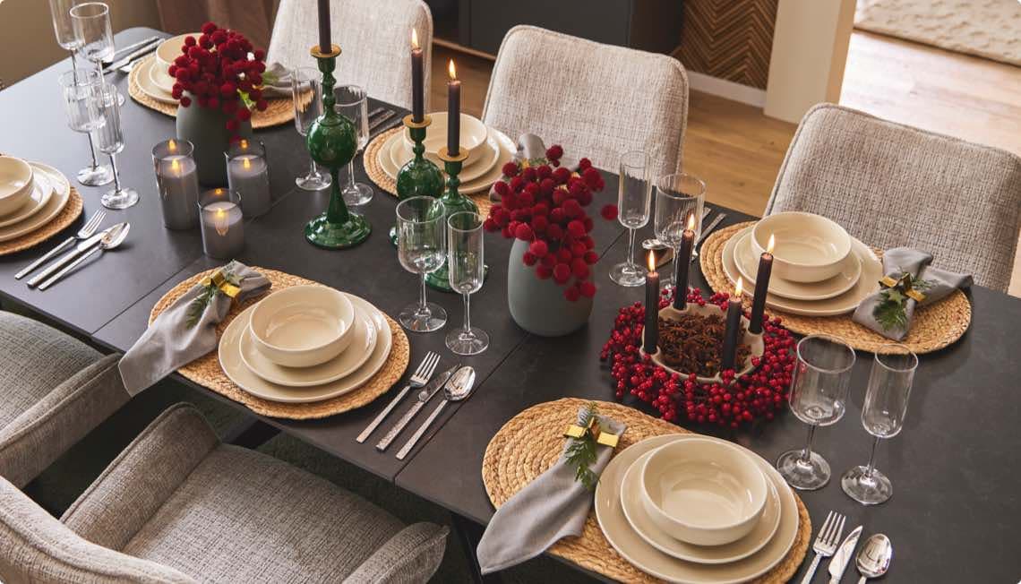 Festlich gedeckter Tisch mit Tellern, Besteck, Gläsern, Kerzen und roten Blumen in Vasen.