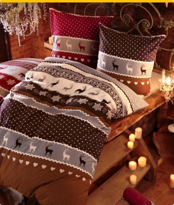 Gemütliches Schlafzimmer mit festlich gemusterter Bettwäsche in Rot, Braun und Weiß, dekoriert mit Kerzen und Pflanzen.