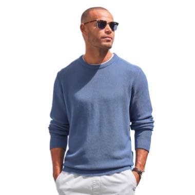 Mann in blauem Pullover und weißer Hose, beide Hände in den Hosentaschen, trägt eine Sonnenbrille
