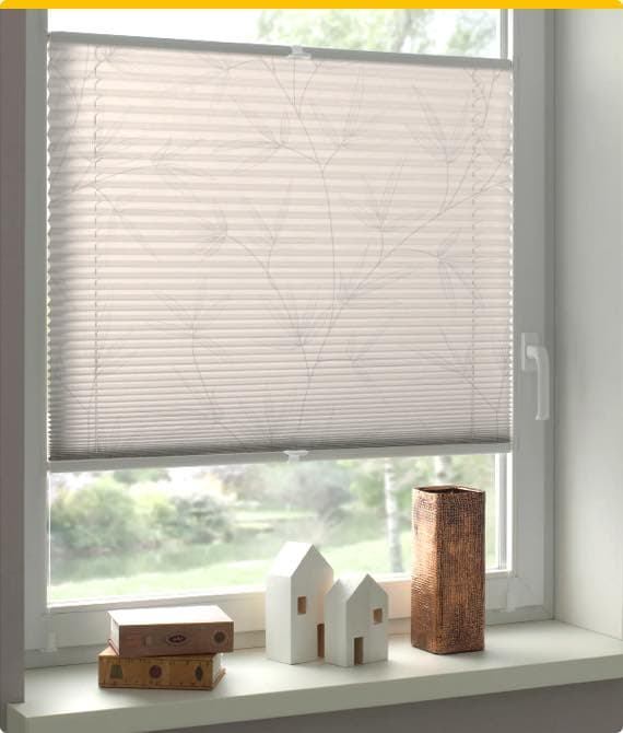 Halb heruntergelassenes Plissee-Rollo mit Blattmuster an einem Fenster, Dekorationen auf der Fensterbank