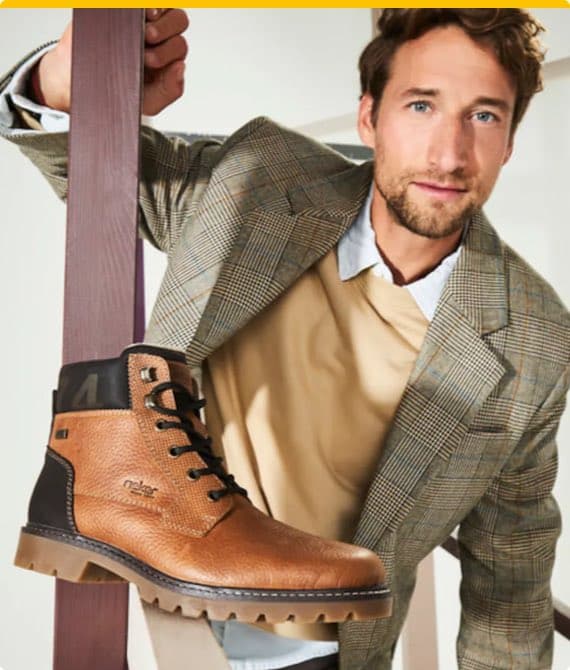 Mann in kariertem Blazer hält braunen Schnürstiefel mit dunklen Details in die Kamera