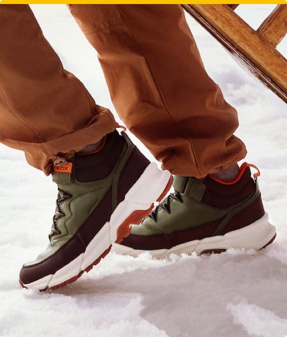 Person trägt grüne Geox-Sneaker mit weißen Sohlen und brauner Hose im Schnee