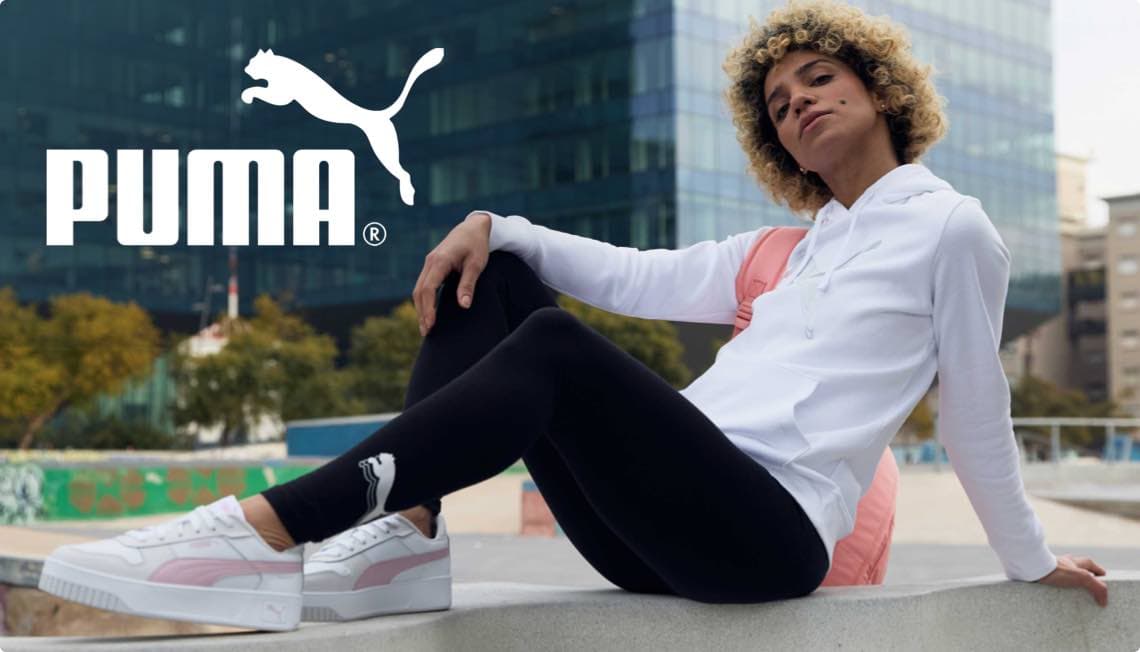 PUMA-Logo – Person in weißem Hoodie und schwarzen Leggings sitzt lässig im Freien.
