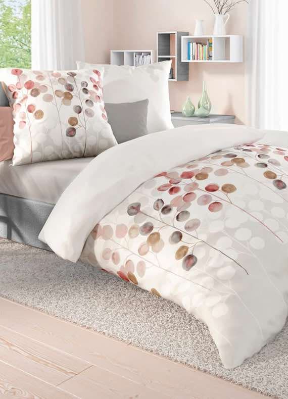 Bett mit weißer Bettwäsche und bunten Blättermotiven, Kissen passend dazu, helles Zimmer mit Regal und Deko.