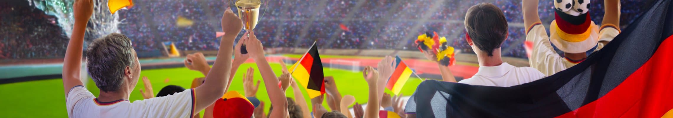 Fans im Stadion jubeln mit Deutschlandfahnen und Pokal, Menschen von hinten vor grünem Spielfeld